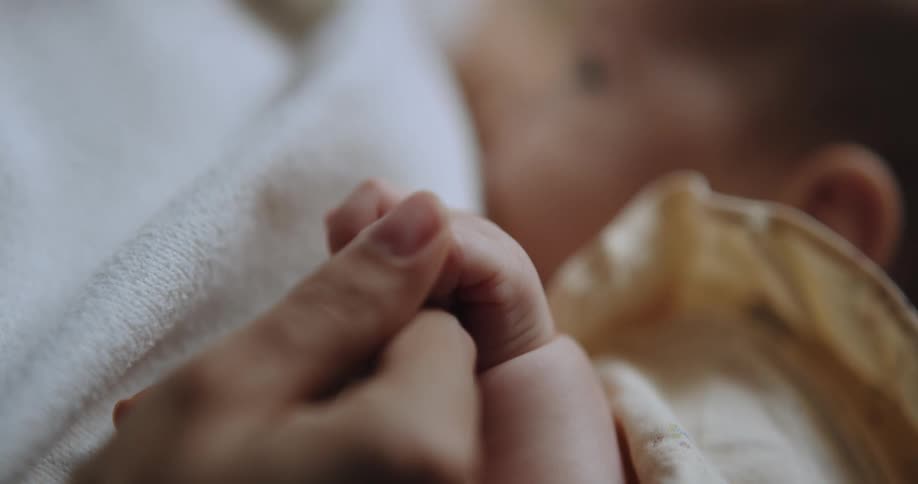 A woman caresses her babys fingers during breastfeeding