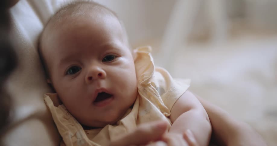 A baby is relaxing in their mothers arms as she holds their hand