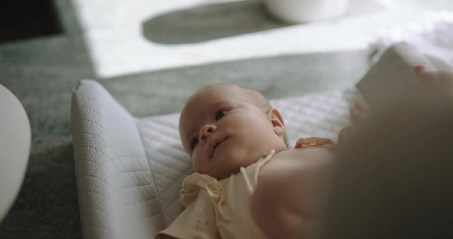 A baby is lying in a crib with their feet in the air as their mother stands over them