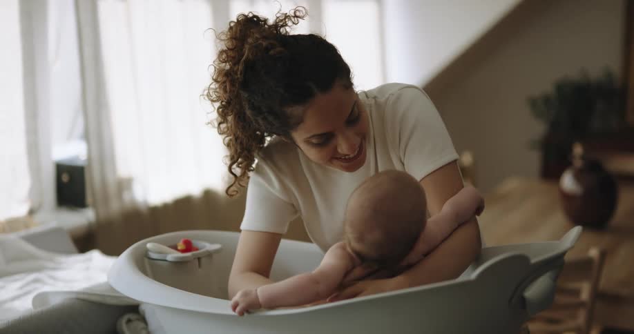 A woman slowly lowers a baby into a baby bath