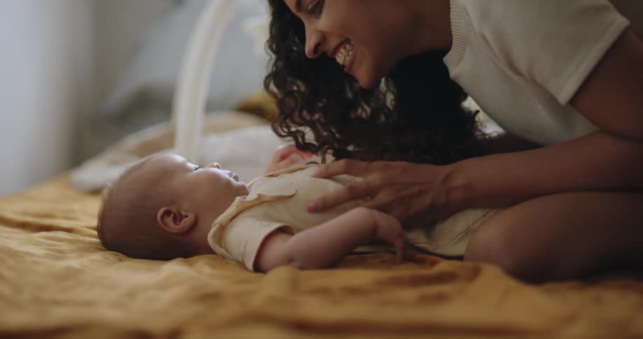 Mom kneeling over baby on a bed tickling and kissing and loving