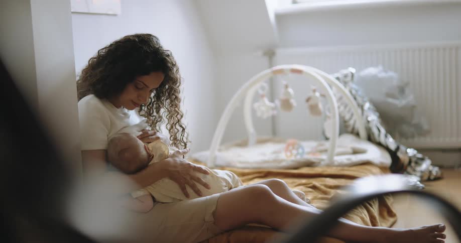 A woman cradles a baby in her lap while sitting on a bed indoors during the day