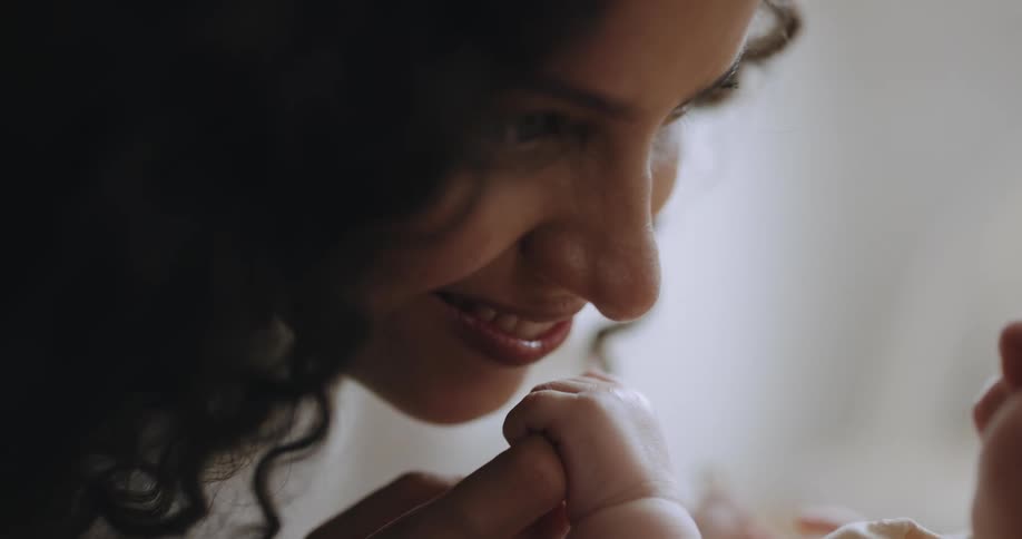 Mother smiles and kisses babys hand