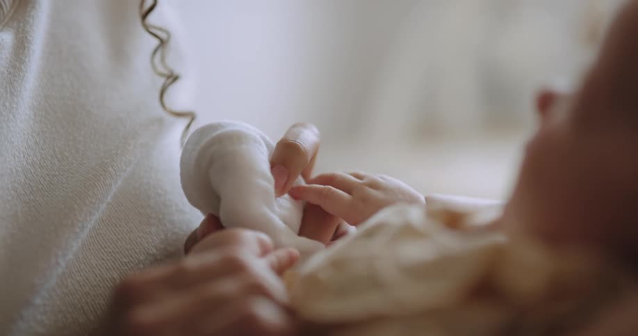Mother with curly hair and white shirt cleans newborn babys mouth
