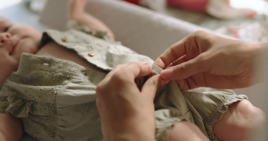 Mom buttons up babys clothing on a changing table