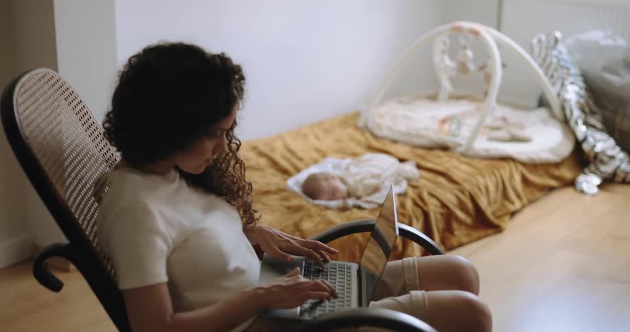 A woman types on her laptop as a baby sleeps