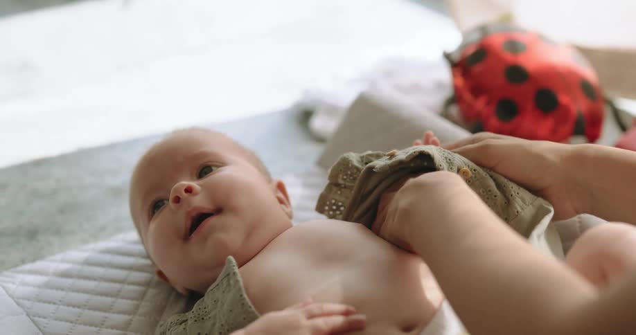 A woman puts a dress on her baby while the girl lies on a bassinet