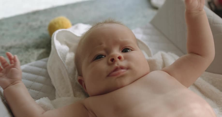 A baby flails its arms while lying on a cushion on the floor