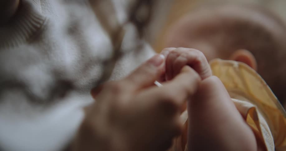 A newborn gripping her mothers finger while breastfeeding