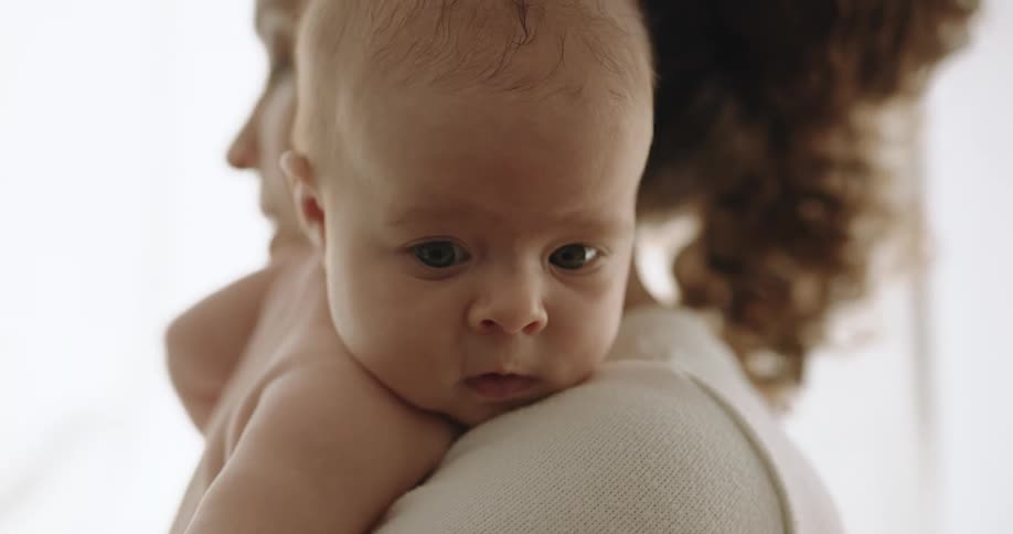 Mother smiles and talks while holding child against her shoulder