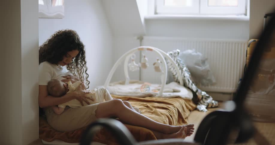 Mother sitting on bed leans against wall and nurses child