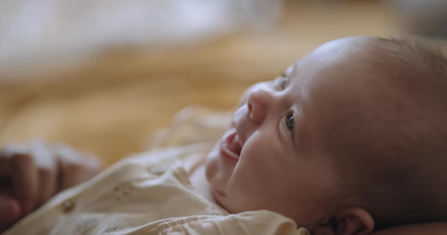 Baby smiles up at mother as woman holds childs hands