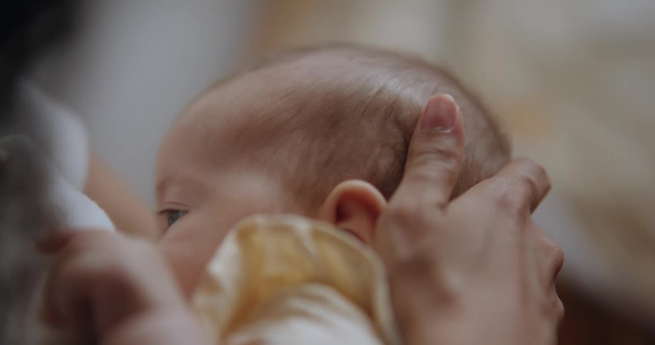 Mother holding her newborn baby close to her chest to breastfeed at home