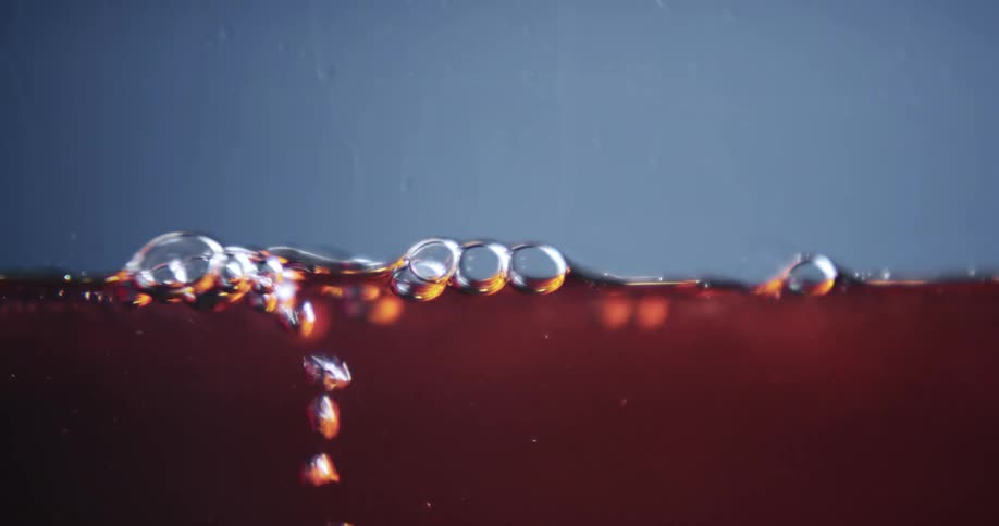 Stream of bubbles rise to surface of reddish liquid against a blueish background