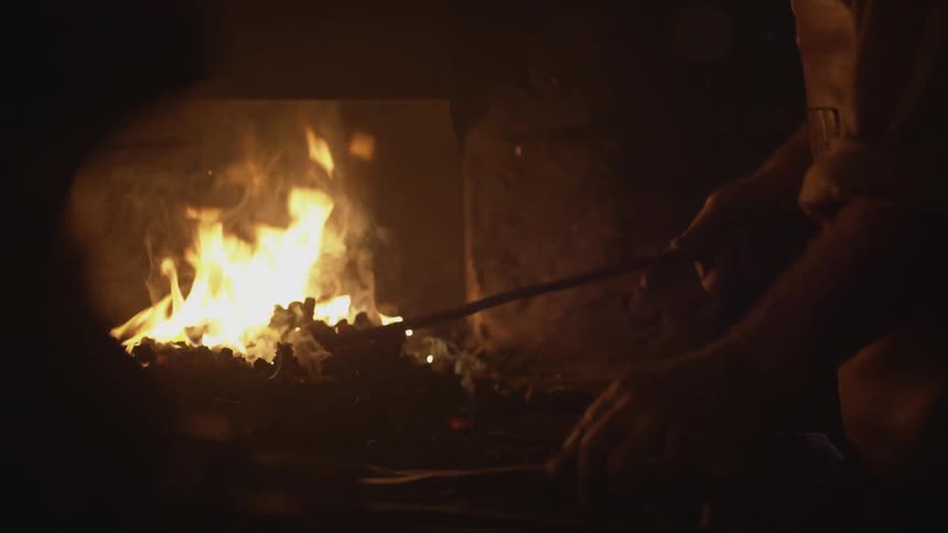 A man stirs a fire with a rod