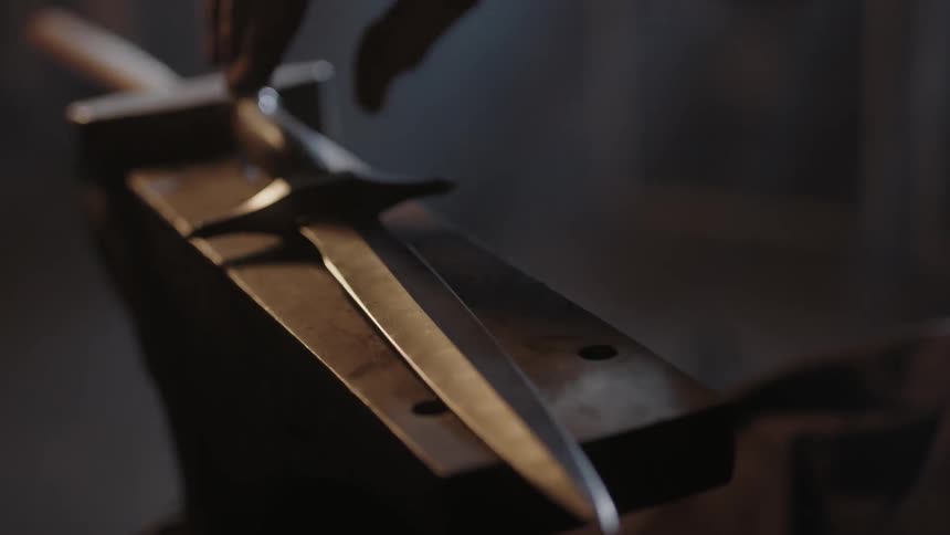 A hand places a dagger down on an anvil