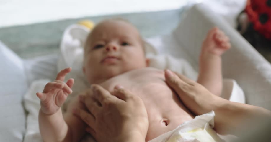 Mother rubs the chest and belly of a baby resting on a crib at home