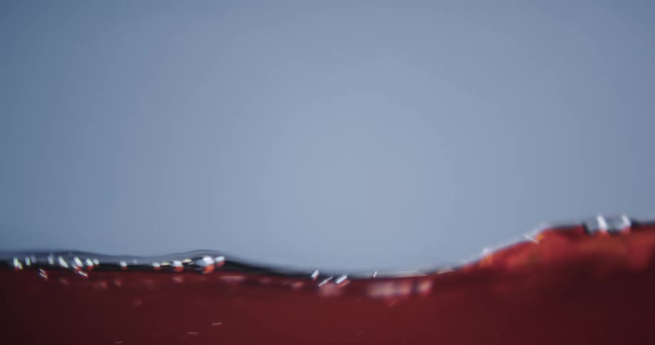 Close up of small waves of red liquid rising and sinking against a blue background