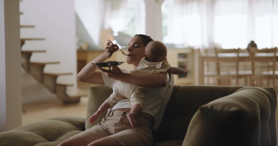 A woman eats as she holds her baby