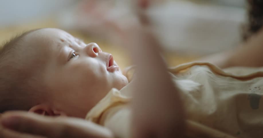 Mother leans over baby as babys moving hand catches mothers long hair