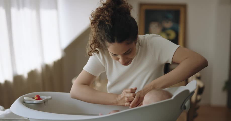 A mom smiles with loves as she bathes and washes her baby in a small tub