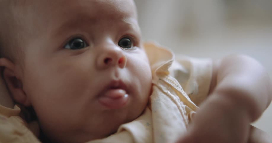 Light shines on the face of a baby as they look around and stick their tongue out