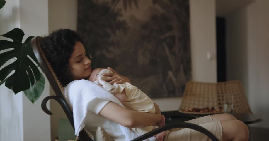 A woman is sitting in a rocking chair and holding her baby in her arms
