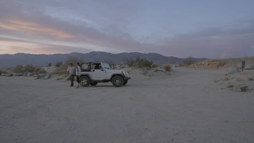 A man and woman exit a jeep stopped in the desert