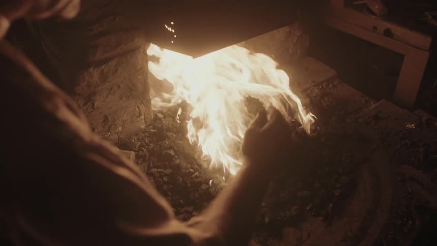 A blacksmith adding coals to a fire