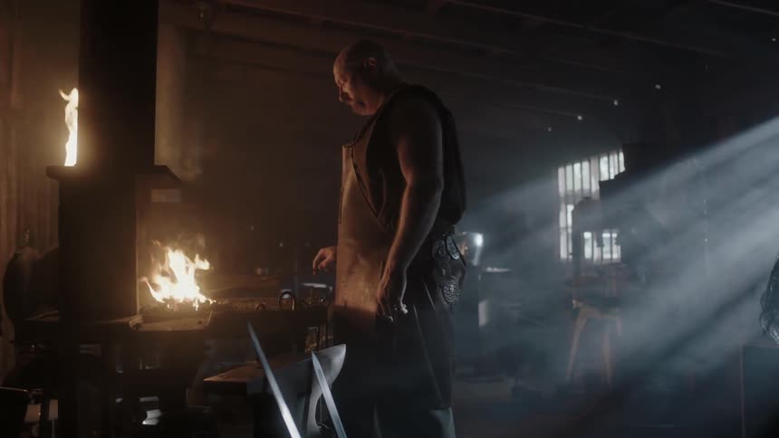 A blacksmith stands before the fire in his shop