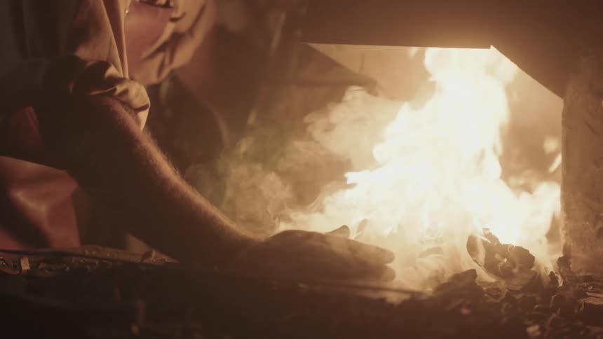 A man arranges the ashes in a fire using his bare hand