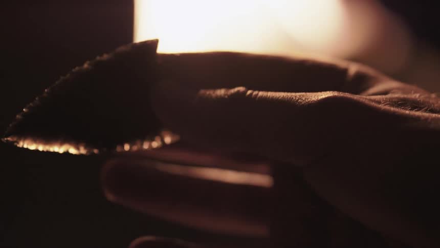 A man studying an arrowhead next to a fire