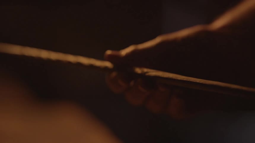 A man runs his fingers down the length of a spear in a dark room