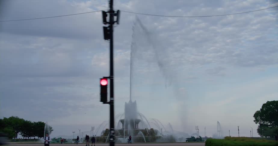 Vehicles drive through an intersection and past a public water fountain in a park