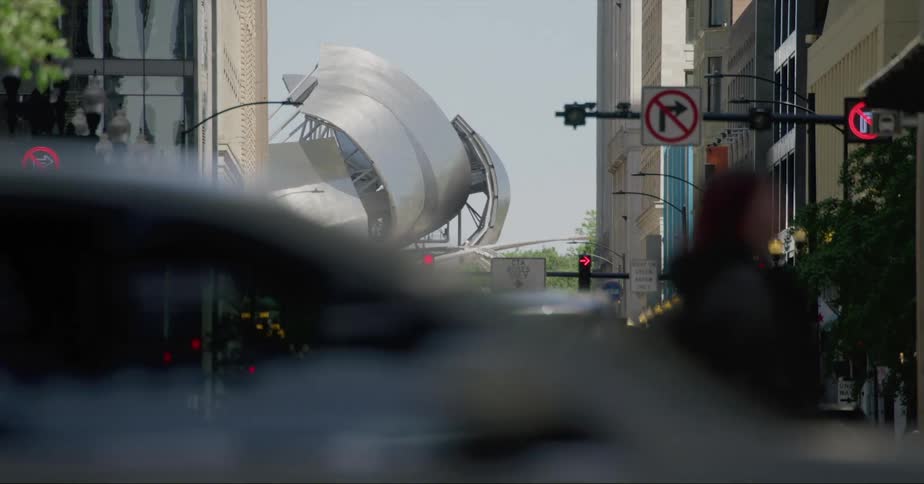 Pedestrians and traffic cross intersections of downtown street leading toward large metal sculpture