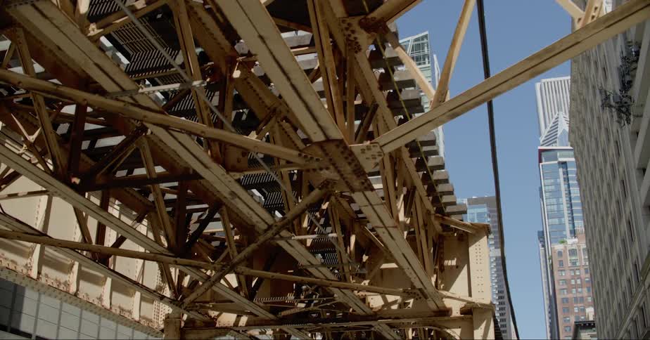Steel beams of an elevated train track with city skyscrapers behind