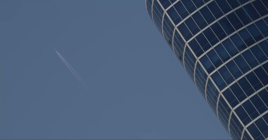 Jet leaves dual contrails as its path roughly parallels a skyscraper