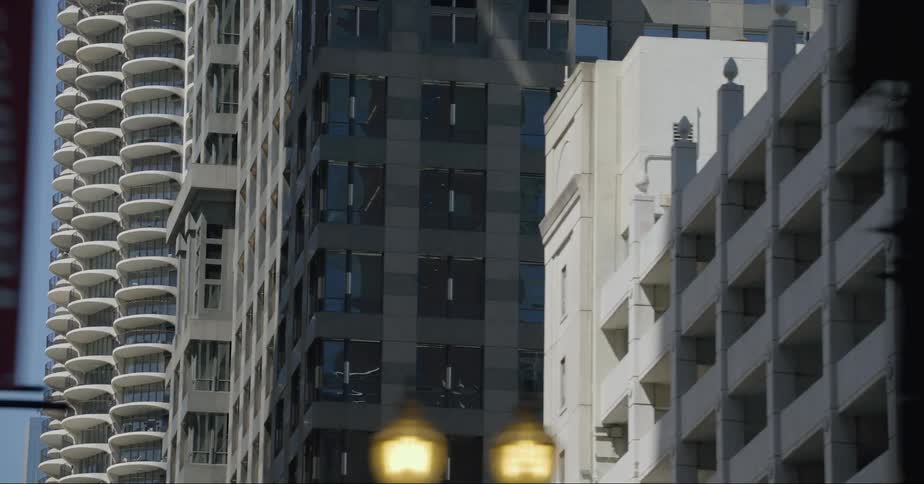 Sunlight shines on tall buildings on a downtown street as traffic lights glow