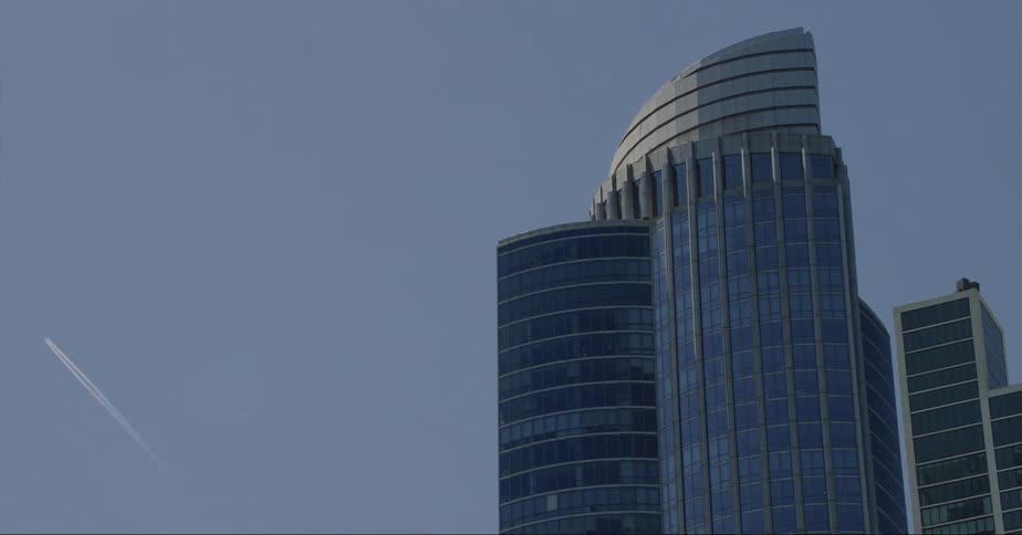 Trail of a plane flying on the blue sky over the skyscrapers in the city skyline at daytime