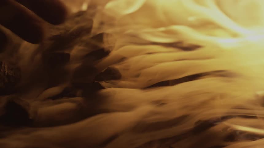 A person mixes rocks in a raging fire