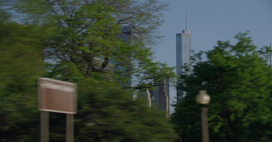 Vehicles drive down a tree lined street with views of downtown