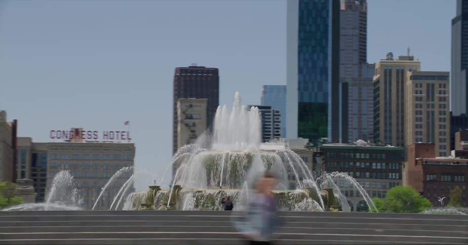 People walk at a park with a fountain in front of high rise office buildings