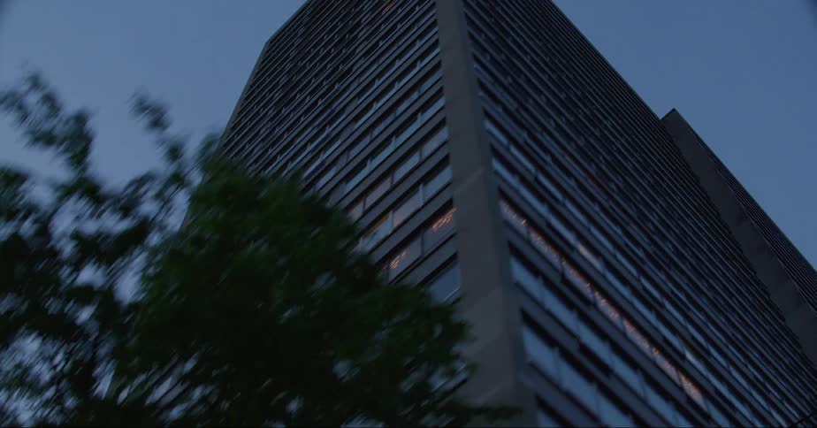 Tall skyscraper seen from a moving vehicle on the street under a deep blue evening sky