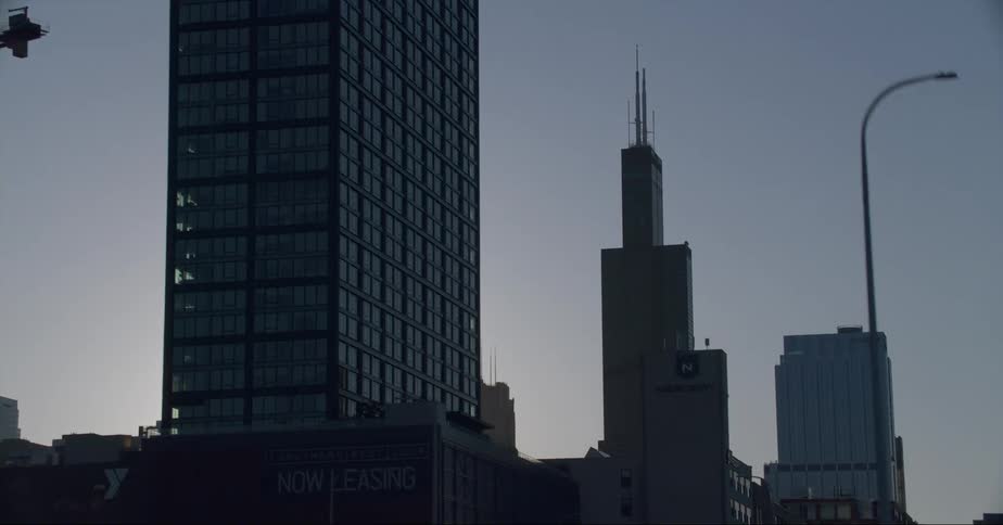 Highway passes under bridge as sun glares past skyscrapers of downtown