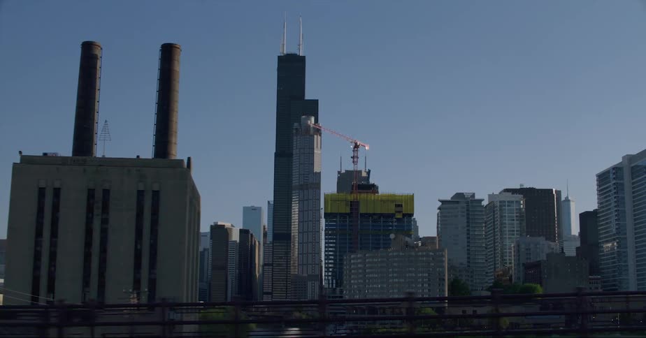 Cars driving past a skyline with office buildings and construction cranes in a city