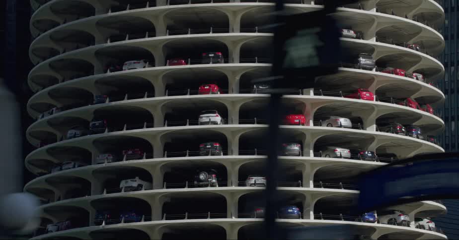Automobiles are parked in a round high rise parking garage near towers and buildings