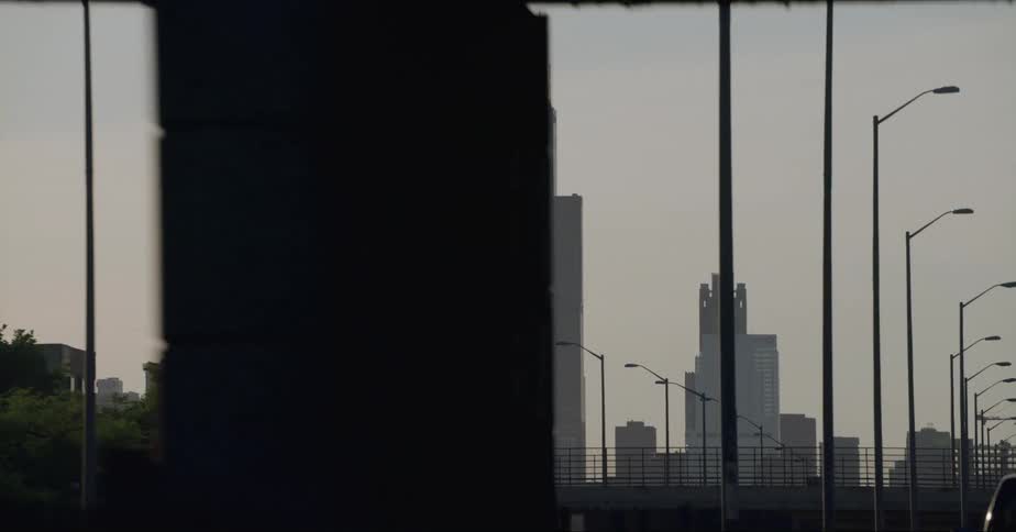 Distant skyscrapers and high rise buildings seen from vehicle driving on highway passing under overpass