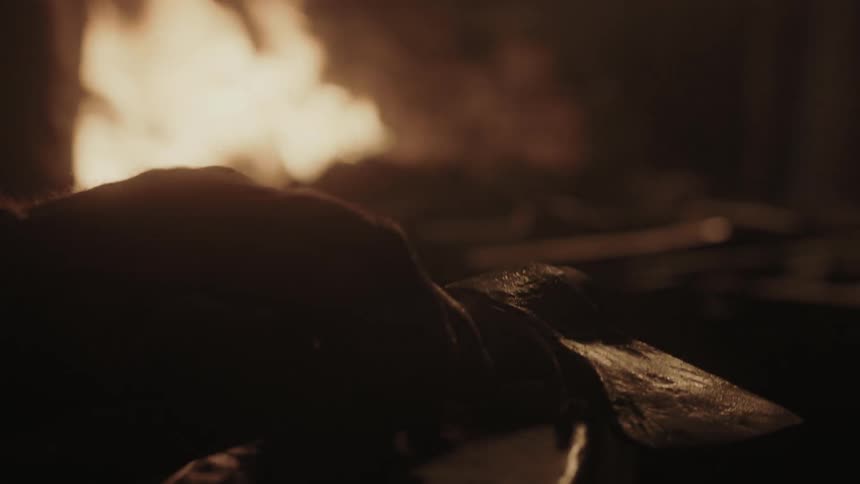 A man lifts an axe from the fire and places it down