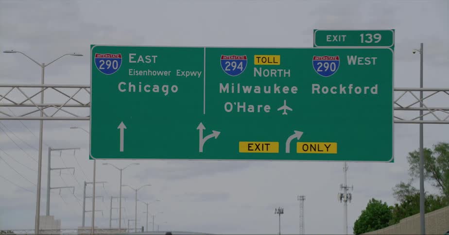 Vehicle drives on highway passing under information sign showing destination