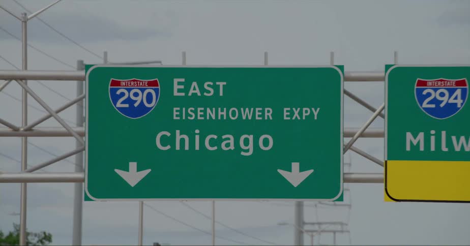 Vehicle drives on highway passing under information sign showing destination